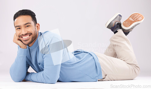 Image of Portrait, happy or Asian man lying on floor isolated on a white background in studio to relax. Friendly smile, calm person or proud male model resting with confidence, fashion or style on the ground