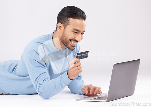 Image of Man, studio and laptop with credit card, e commerce or payment information with smile by white background. Young asian guy, floor and happy with fintech, sale or deal with virtual customer experience