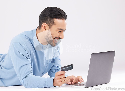 Image of Laptop, credit card and happy asian man on studio floor for ecommerce, sale or cashback on grey background. Online shopping, deal and Japanese male customer smile for loan, payment or sign up promo