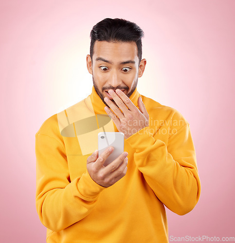 Image of Phone, wow or gossip with a surprised man in studio on pink background reading fake news announcement online. Mobile, shock and wtf with a young male person on a social media website or the internet