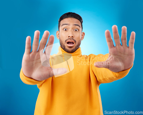 Image of Stop, hands and portrait of asian man in studio with warning, danger and wait sign on blue background. Face, palm and Japanese male model with caution, fear of surprise, drama or block conflict