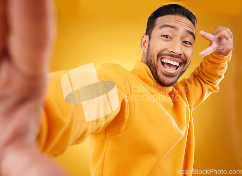 Image of Peace sign, selfie and happy portrait of a man in studio with a hand, emoji and a smile. Male asian fashion model excited on a yellow background with a positive icon for social media profile picture