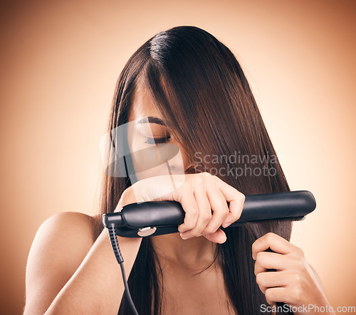 Image of Young woman, hair care and flat iron in studio to straightener for healthy shine and growth. Young female aesthetic model on a brown background with hot tools for hairstyle, cosmetics and beauty