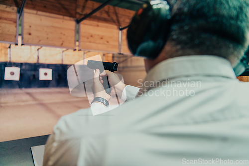 Image of A man practices shooting a pistol in a shooting range while wearing protective headphones