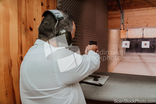 Image of A man practices shooting a pistol in a shooting range while wearing protective headphones