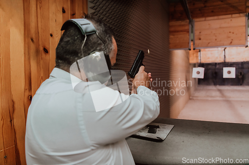 Image of A man practices shooting a pistol in a shooting range while wearing protective headphones