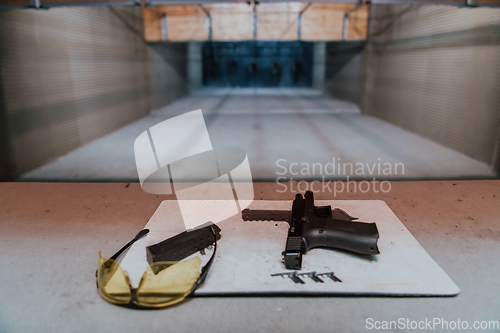 Image of Shooting equipment in front of the target. Pistol, goggles and headphones on the table of a modern shooting range