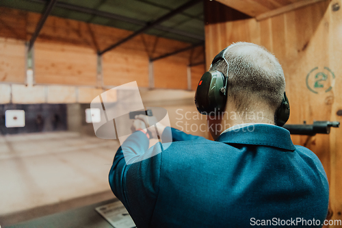 Image of A man practices shooting a pistol in a shooting range while wearing protective headphones