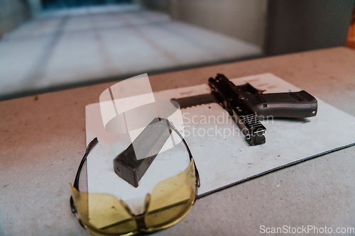 Image of Shooting equipment in front of the target. Pistol, goggles and headphones on the table of a modern shooting range