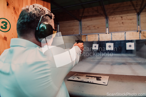 Image of A man practices shooting a pistol in a shooting range while wearing protective headphones