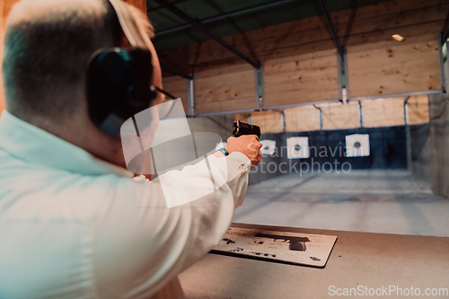 Image of A man practices shooting a pistol in a shooting range while wearing protective headphones