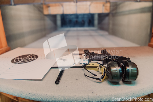 Image of Shooting equipment in front of the target. Pistol, goggles and headphones on the table of a modern shooting range
