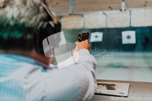 Image of A man practices shooting a pistol in a shooting range while wearing protective headphones