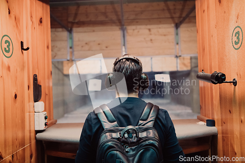 Image of A man practices shooting a pistol in a shooting range while wearing protective headphones