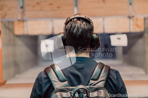 Image of A man practices shooting a pistol in a shooting range while wearing protective headphones