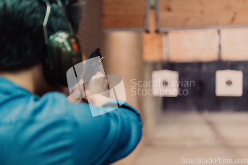 Image of A man practices shooting a pistol in a shooting range while wearing protective headphones