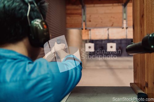 Image of A man practices shooting a pistol in a shooting range while wearing protective headphones