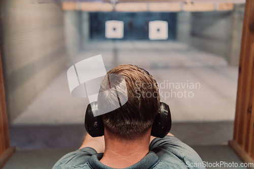 Image of A man practices shooting a pistol in a shooting range while wearing protective headphones