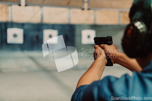 Image of A man practices shooting a pistol in a shooting range while wearing protective headphones