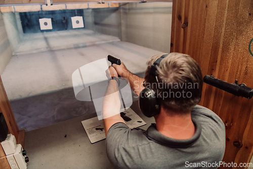 Image of A man practices shooting a pistol in a shooting range while wearing protective headphones