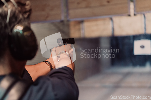 Image of A man practices shooting a pistol in a shooting range while wearing protective headphones