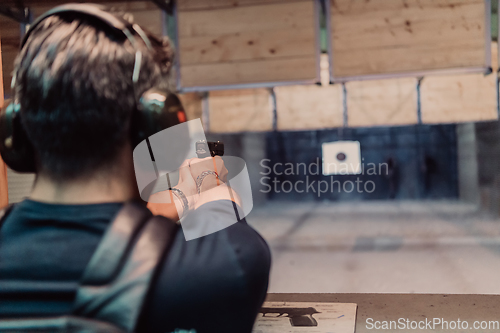 Image of A man practices shooting a pistol in a shooting range while wearing protective headphones