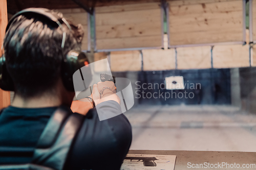 Image of A man practices shooting a pistol in a shooting range while wearing protective headphones