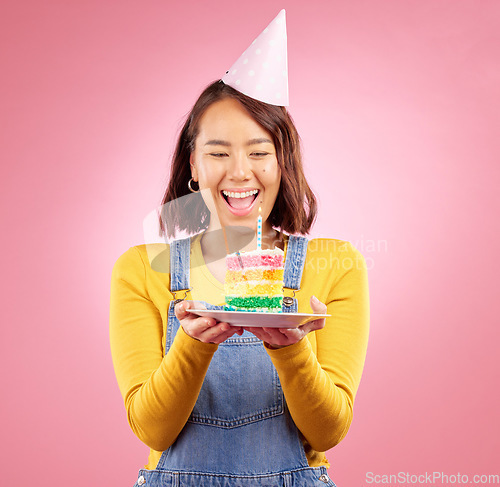 Image of Birthday cake candle, celebration and Asian woman excited, smile and celebrate party, surprise or studio gift. Event cheers, wow and Japanese person with dessert, candy or sweets on pink background