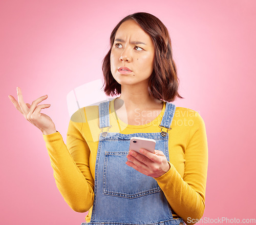 Image of Confused, studio and Asian woman with smartphone problem, 404 fail and stress over mistake, error or ideas. Thinking, doubt and Japanese person frustrated over online phone glitch on pink background