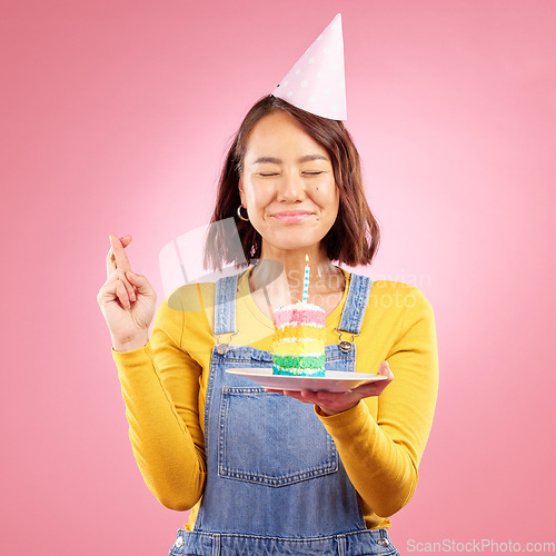 Image of Birthday cake candle, wish and Asian woman with fingers crossed, hope and celebrate party, present or studio gift. Praying, emoji icon sign and person with dessert, candy or sweets on pink background