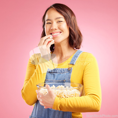 Image of Portrait, woman and eating popcorn in studio for watching movie, film or cinema show on pink background. Happy young asian model, bowl and snack to enjoy streaming, subscription and tv entertainment