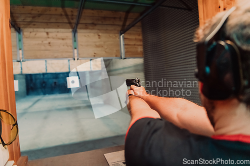 Image of A man practices shooting a pistol in a shooting range while wearing protective headphones