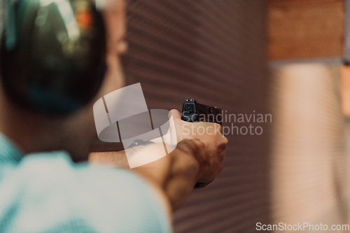 Image of A man practices shooting a pistol in a shooting range while wearing protective headphones