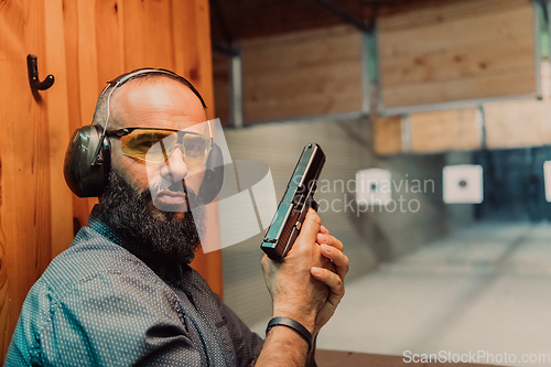 Image of A man practices shooting a pistol in a shooting range while wearing protective headphones