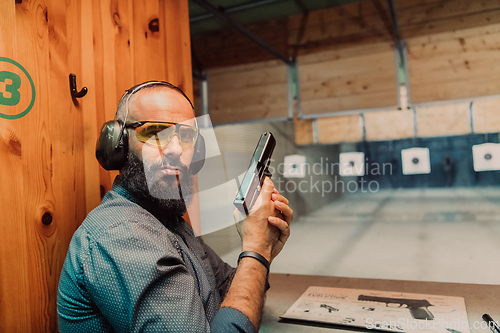 Image of A man practices shooting a pistol in a shooting range while wearing protective headphones