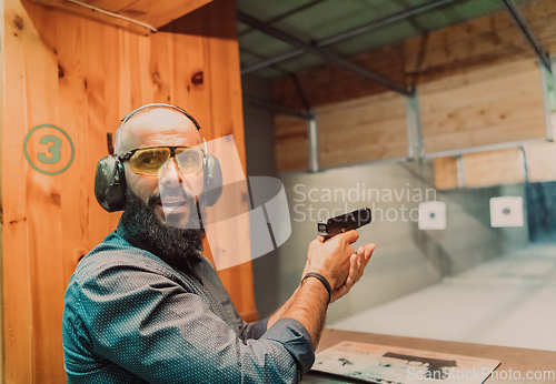 Image of A man practices shooting a pistol in a shooting range while wearing protective headphones