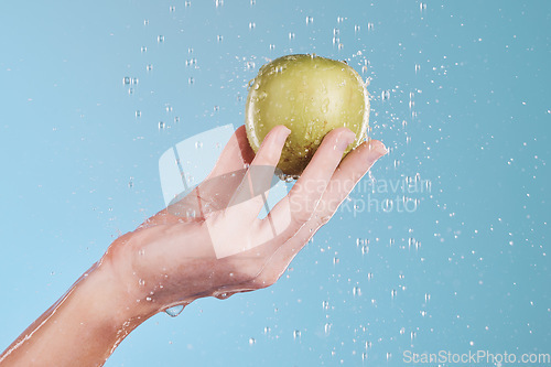 Image of Apple, cleaning and hand with water drops for wellness and skincare in a studio. Isolated, blue background and nutrition for dermatology, splash and health food with fruit for a diet and healthcare