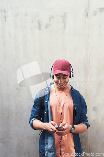 Image of Happy, headphones and man with phone on a wall for social media, communication or a chat. Smile, technology and a male college student streaming or listening to a podcast on a mobile app with mockup