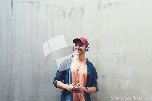 Image of Man, listening and music with smile in outdoor with concrete wall background for entertainment. Happy, face and guy with headphones is excited with tech for streaming radio with student for sound.
