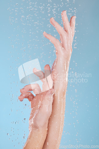 Image of Water drops, skin and person washing hands in studio on blue background for hygiene or hydration. Cleaning, wellness and skincare with a woman in the bathroom for sustainability or to remove bacteria