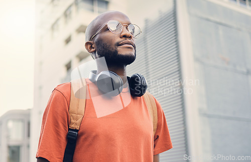 Image of .Black man, student and walking outdoor on a city street while thinking of music and freedom. A serious African person with a backpack on an urban road with casual style and fashion for travel.