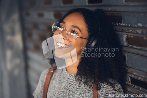 Image of .Thinking, music and smile with a woman in the city, streaming or listening to the radio using headphones. Face, idea and audio with a happy young female person hearing sound in an urban town.