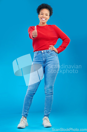 Image of Happy woman, portrait and thumbs up for approval, winning or success against a blue studio background. Female person smile in casual fashion with like emoji, yes sign or OK for agreement or thank you