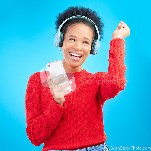 Image of Happy woman, headphones and listening to music for audio streaming against a blue studio background. Excited female person dancing and enjoying sound track or entertainment with mobile smartphone