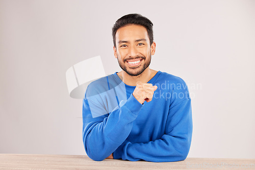 Image of Smile, table and portrait of a man happy to relax on a desk feeling confident isolated in a studio white background. Resting, calm and young male person looking handsome, friendly and with style