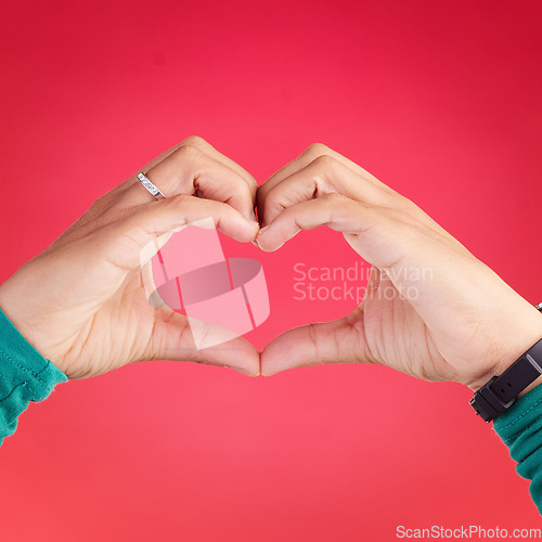 Image of Closeup, person and heart hands for love, care or compassion against a red studio background. Hand together in loving emoji, shape or symbol for romantic gesture, icon or valentines day