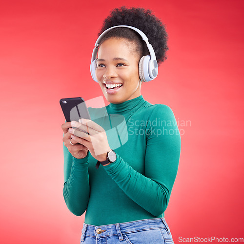 Image of Happy woman, phone and listening to music on headphones against a red studio background. African female person smile with headset in audio streaming, entertainment or sound track on mobile smartphone