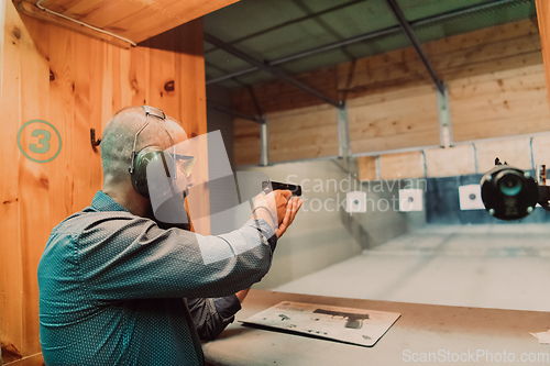 Image of A man practices shooting a pistol in a shooting range while wearing protective headphones