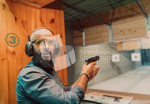 Image of A man practices shooting a pistol in a shooting range while wearing protective headphones