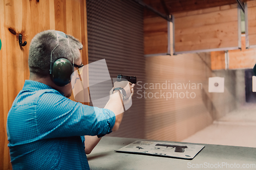 Image of A man practices shooting a pistol in a shooting range while wearing protective headphones